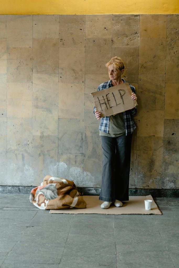pexels-photo-8078413-8078413 An elderly woman stands holding a cardboard sign that reads 'HELP,' conveying a sense of homelessness and need.
